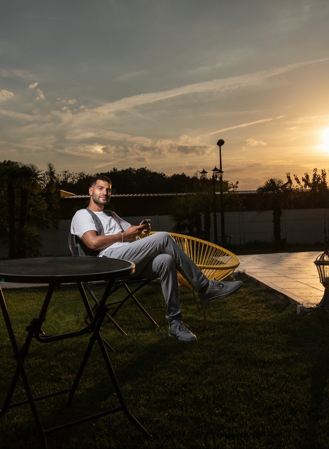 Vidéaste de mariage professionnel assis sur une chaise, regard fier vers l’objectif, avec un coucher de soleil en arrière-plan.